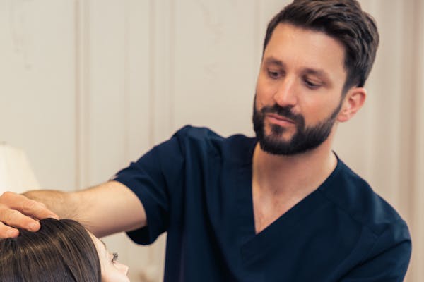 Le praticien Alexandre Mertens, en consultation avec une patiente pour une rhinoplastie. Examine le nez de la patiente.