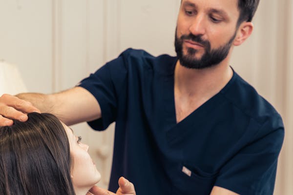 Praticien qui analyse le visage d'une patiente dans le cadre d'injections d'acide hyaluronique.