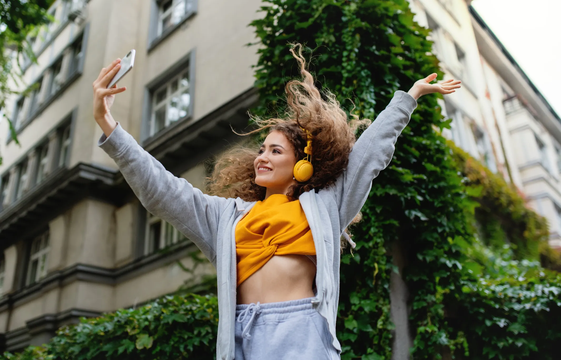 Jovem dançando na rua enquanto usa o celular, gravando um vídeo para redes sociais