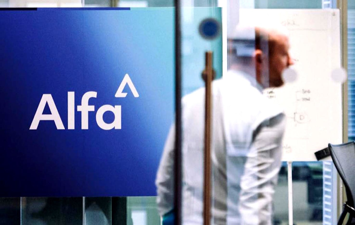 Man walking behind glass door and passing the Alfa logo