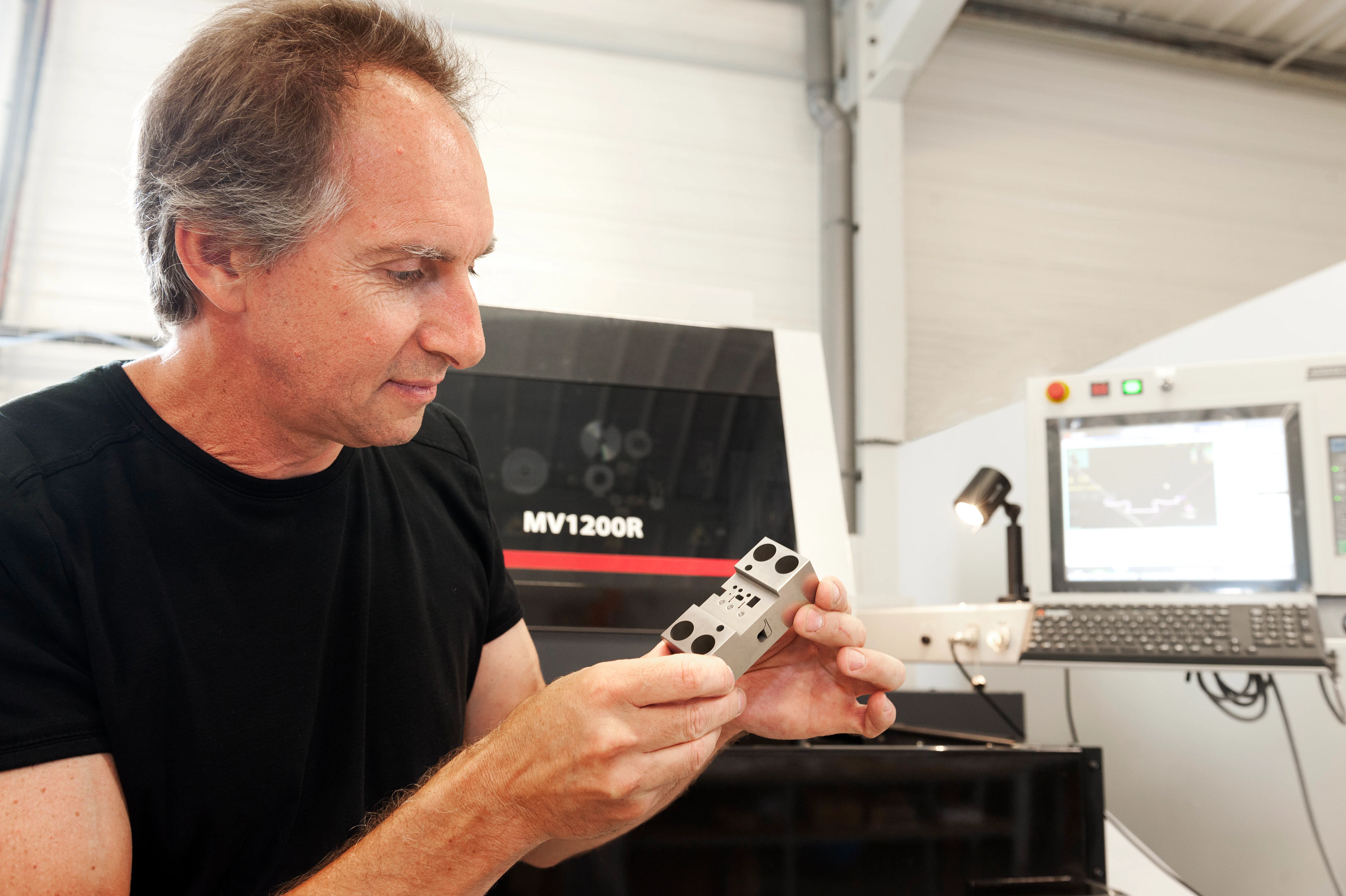 Personne présentant un produit usiné devant une machine