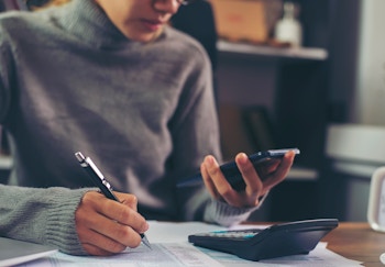 person looking at a phone and calculator while writing