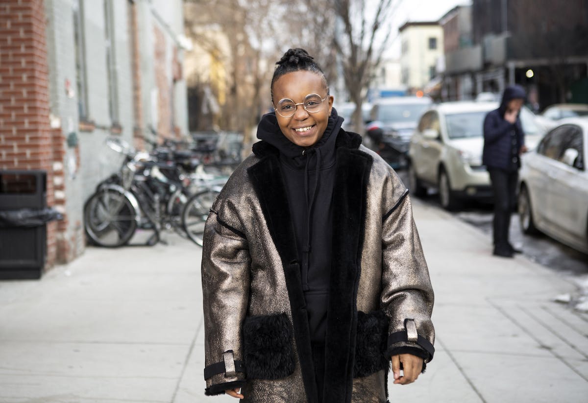 A transmasculine person in a winter coat on the sidewalk