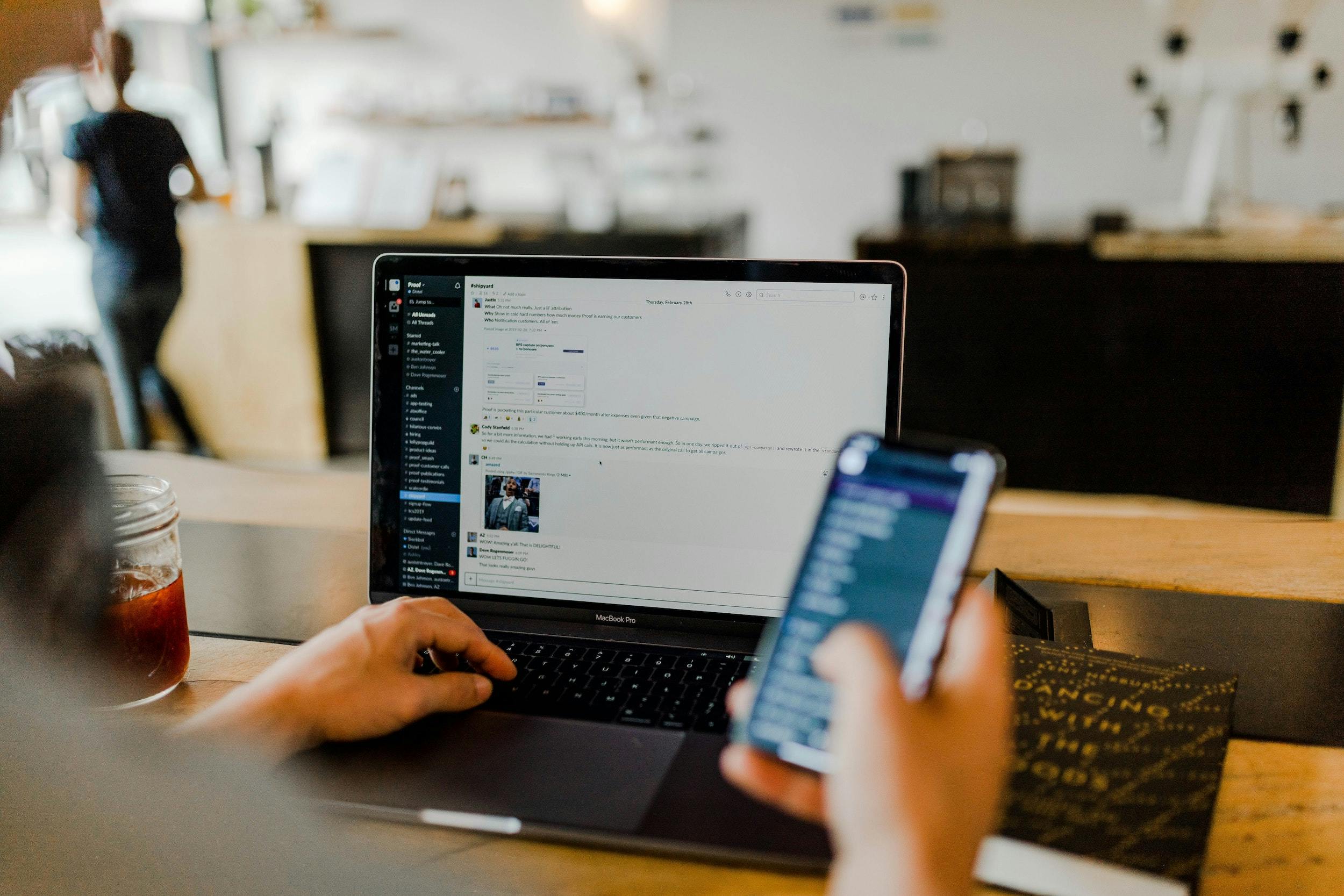 person using Slack on computer and phone simultaneously