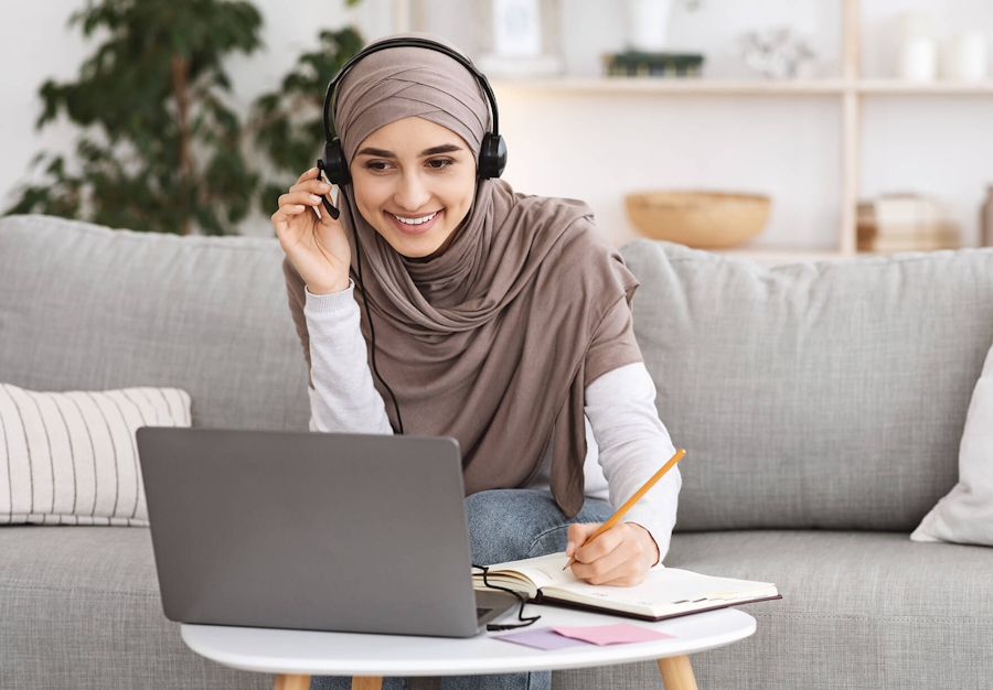 A woman wearing hijab working happily on her laptop