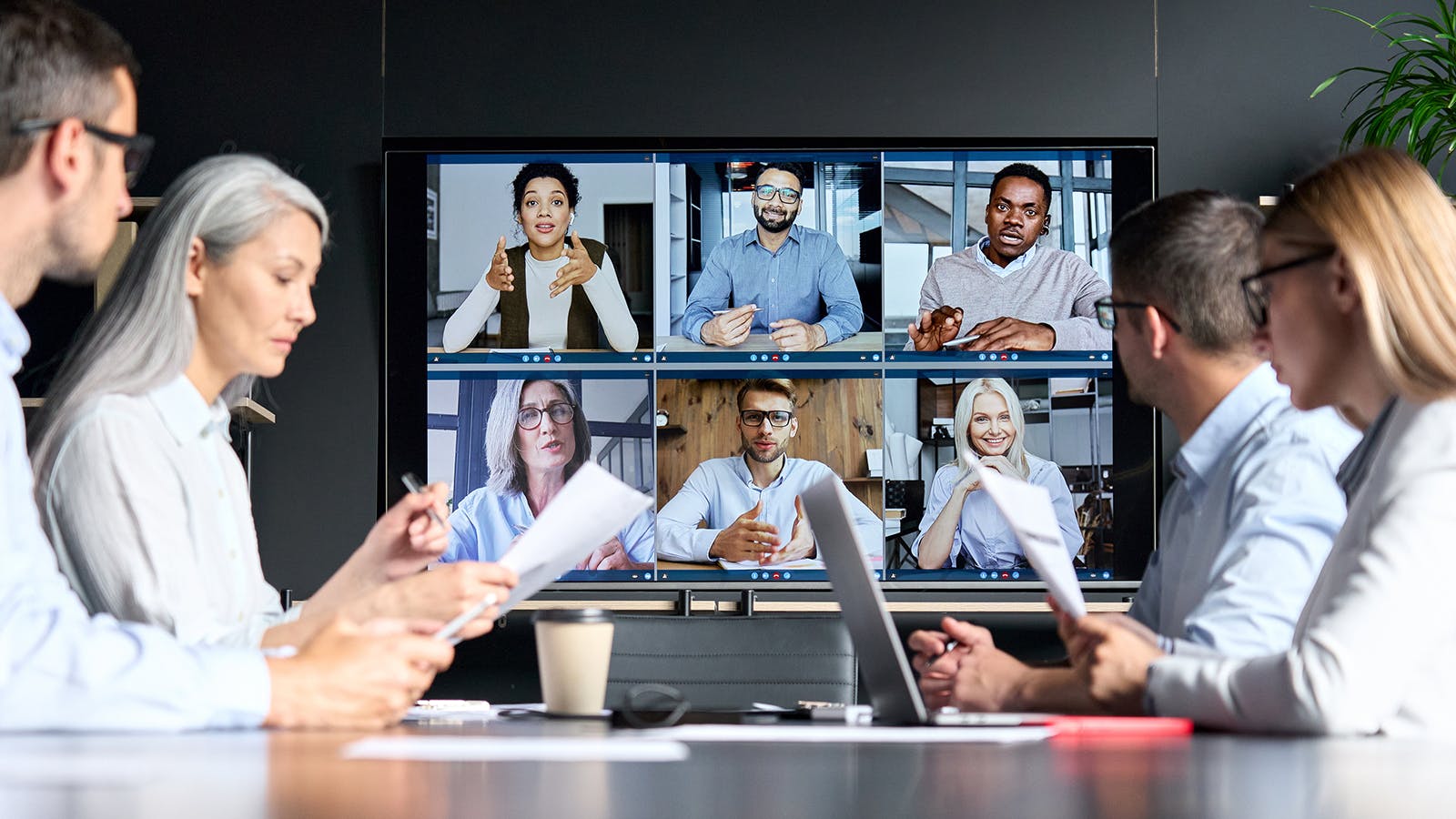 A hybrid HR work team pictured in an office on a video call with a remote team of six employees