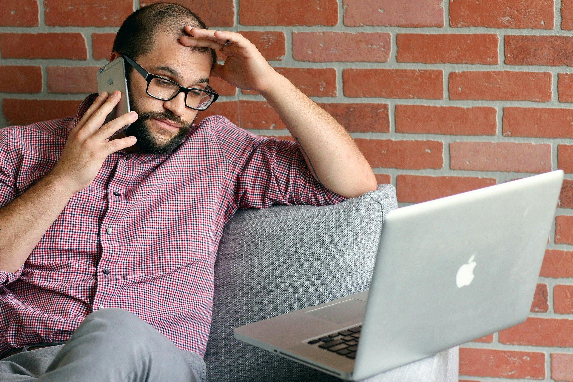 Man looking annoyed talking on the phone next to his laptop