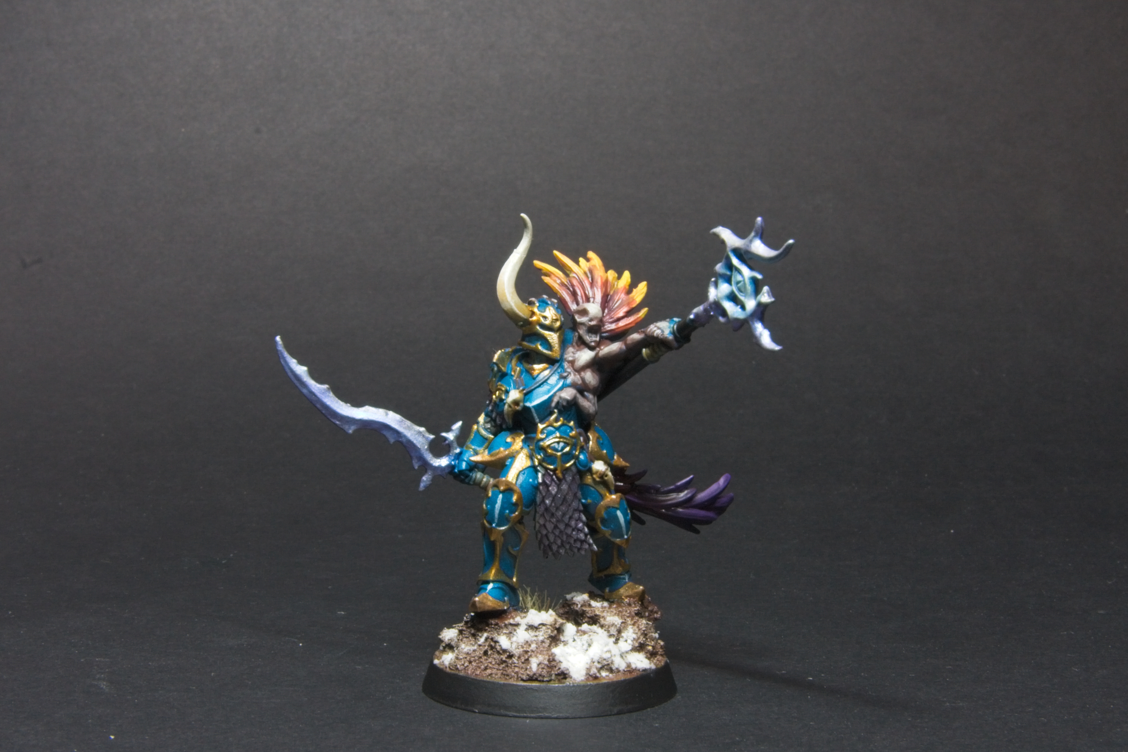 A chaos warrior in teal and gold army, with a Curseling that has red to yellow feathers. 