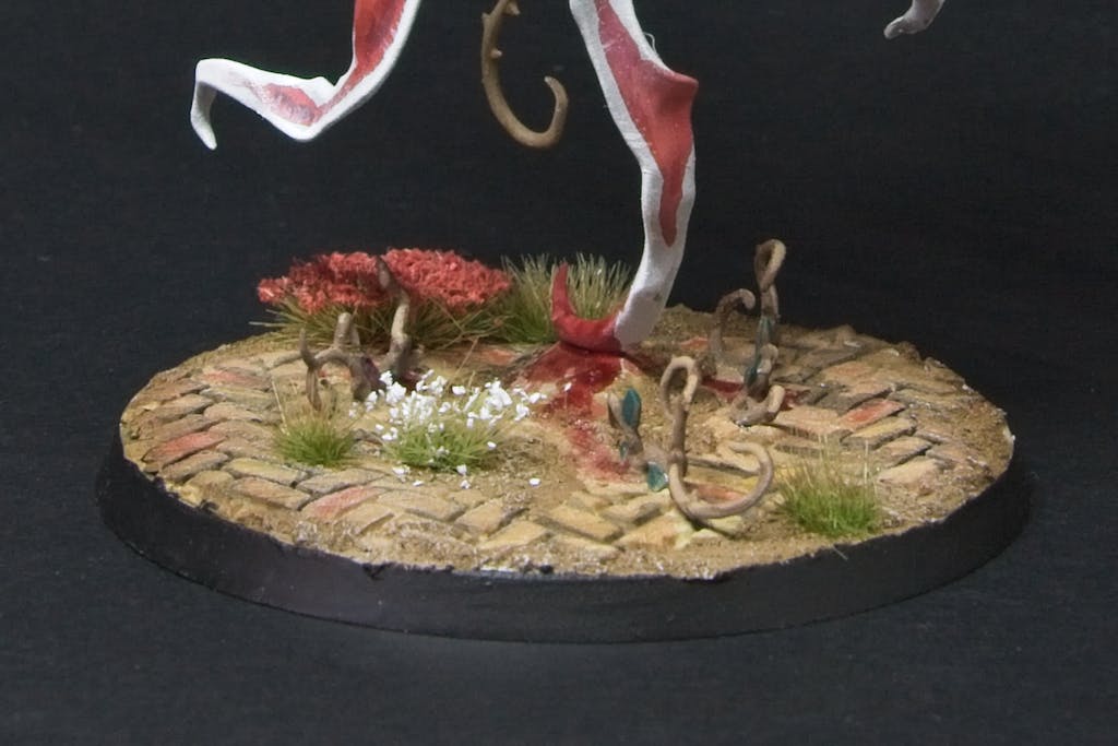 The mini's base, with a stone tiled ground, bloody trails leading to vines, and white/red flowers.