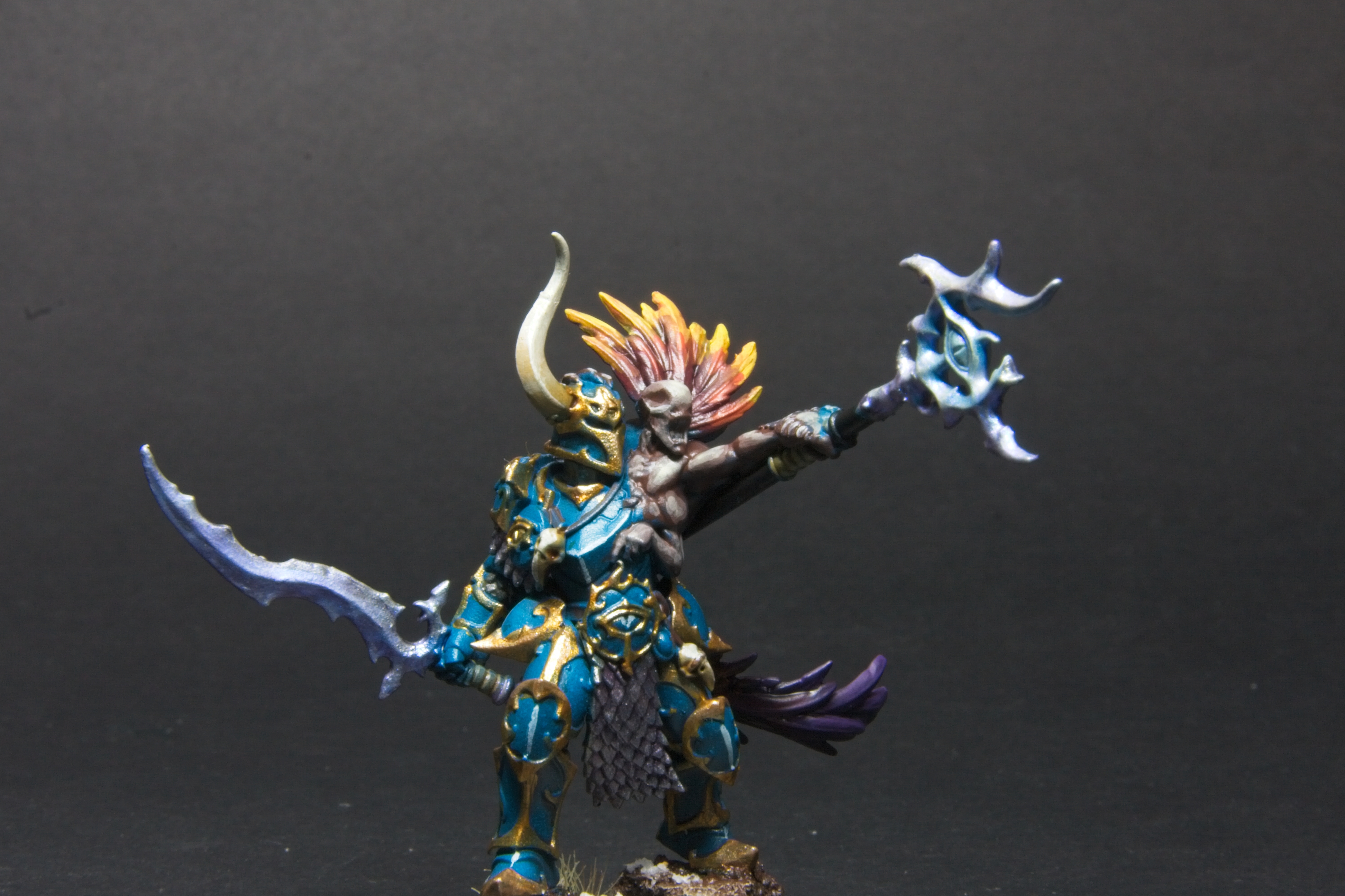 A chaos warrior in teal and gold army, with a Curseling that has red to yellow feathers. 