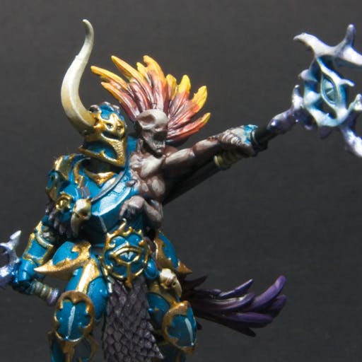 A chaos warrior in teal and gold army, with a Curseling that has red to yellow feathers. 