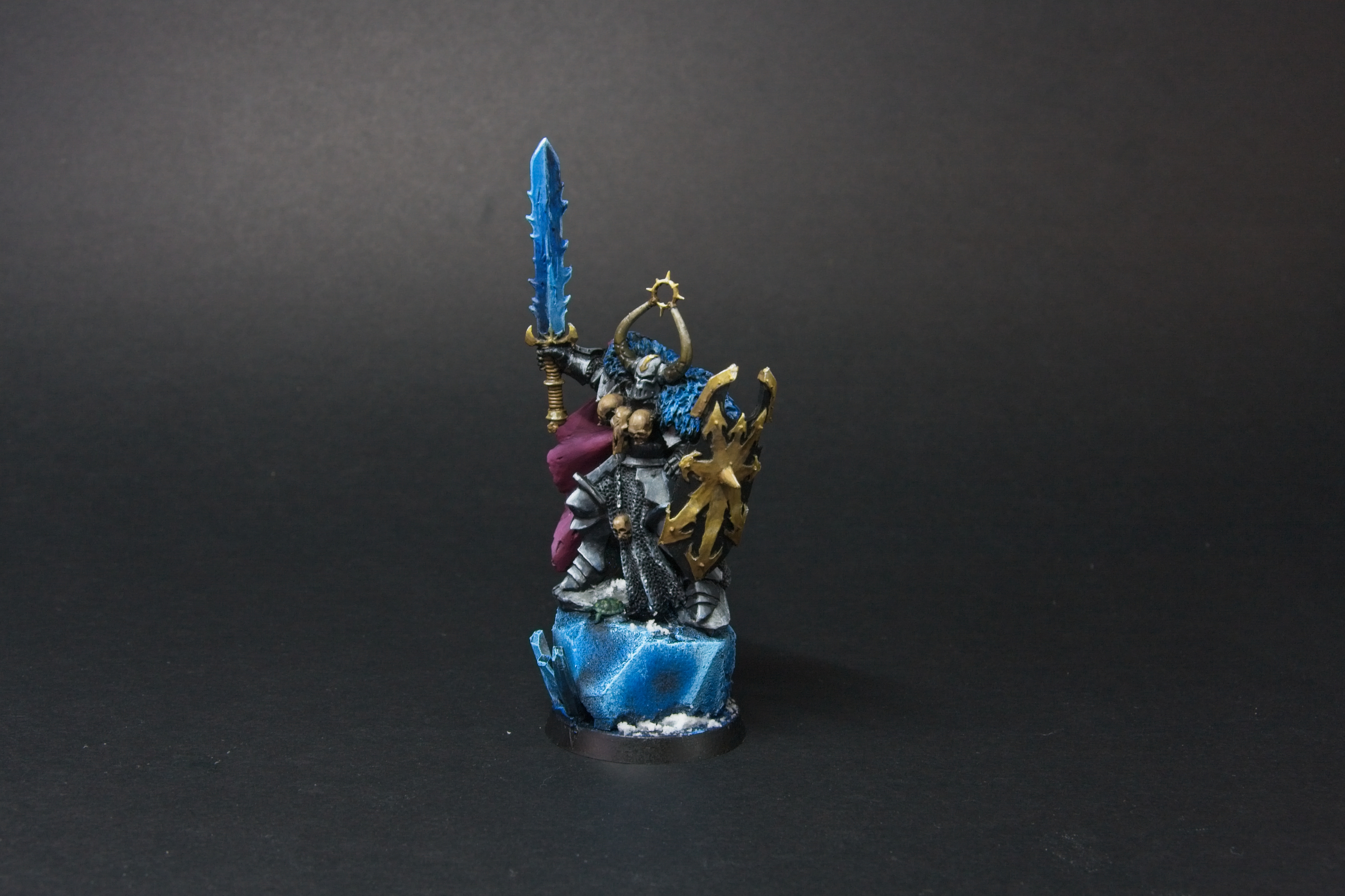 Old metal archon, with three skulls at his chest, a mauve cape, a blue sword, and a golden shield.