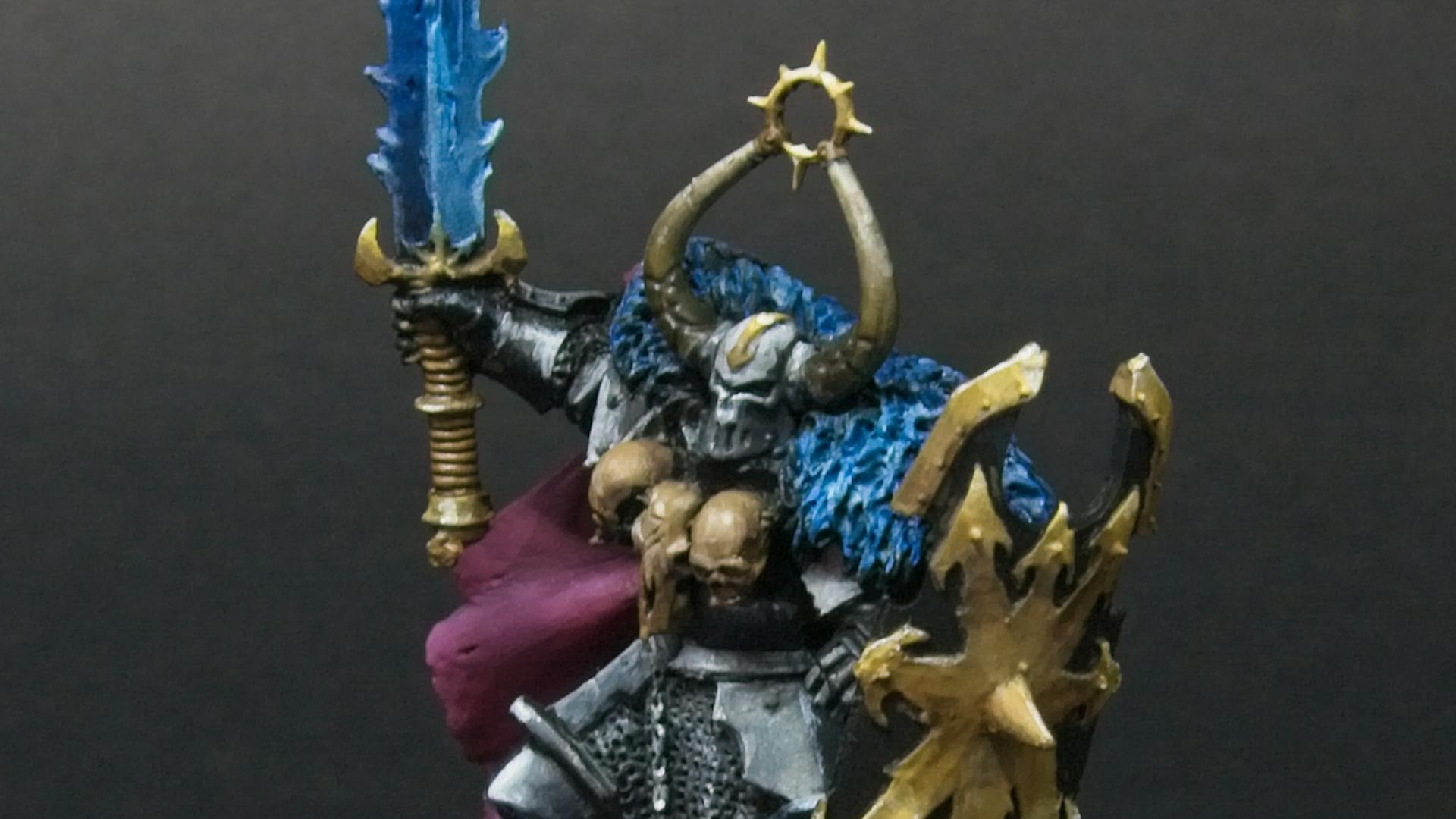 Old metal archon, with three skulls at his chest, a mauve cape, a blue sword, and a golden shield.