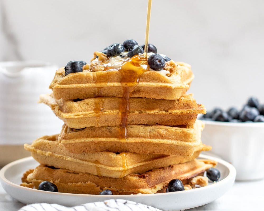 large stack of waffles with blueberries and syrup on