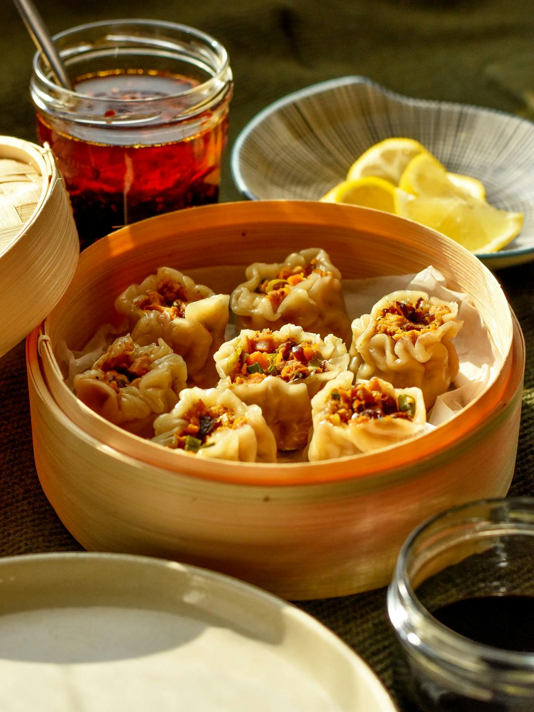 vegan filipino siomai in a bamboo steamer served with garlic chilli oil, lemon wedges and soy sauce