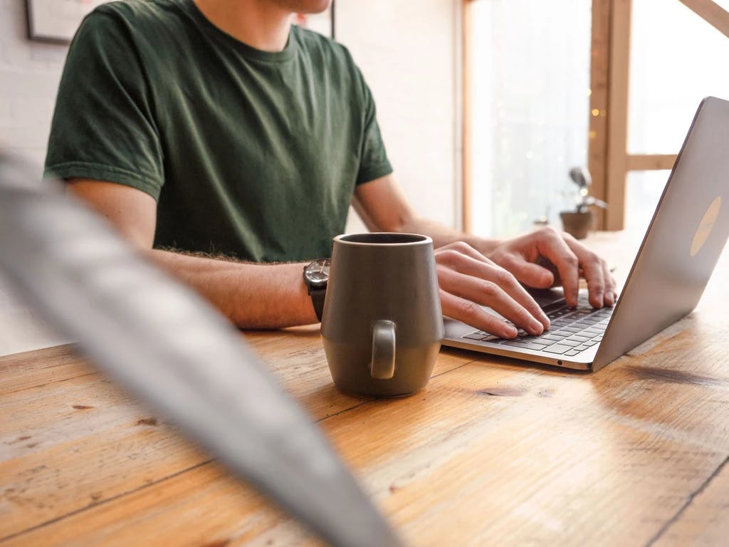 Image of Barney typing into his laptop. Zoomed in shot of just his torso, the laptop and a mug of coffee stood just to the side of his laptop.