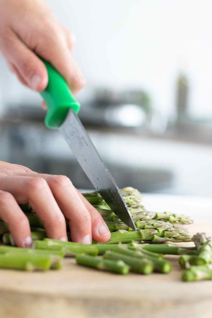 Close up image of some asparagus being chopped by Joey. You can see her holding some asparagus down on a chopping board and she's about to chop the heads off with a knife.