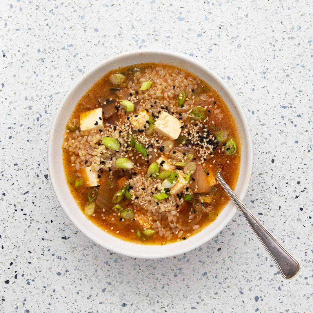 kimchi brown rice and tofu soup in white bowl with spoon