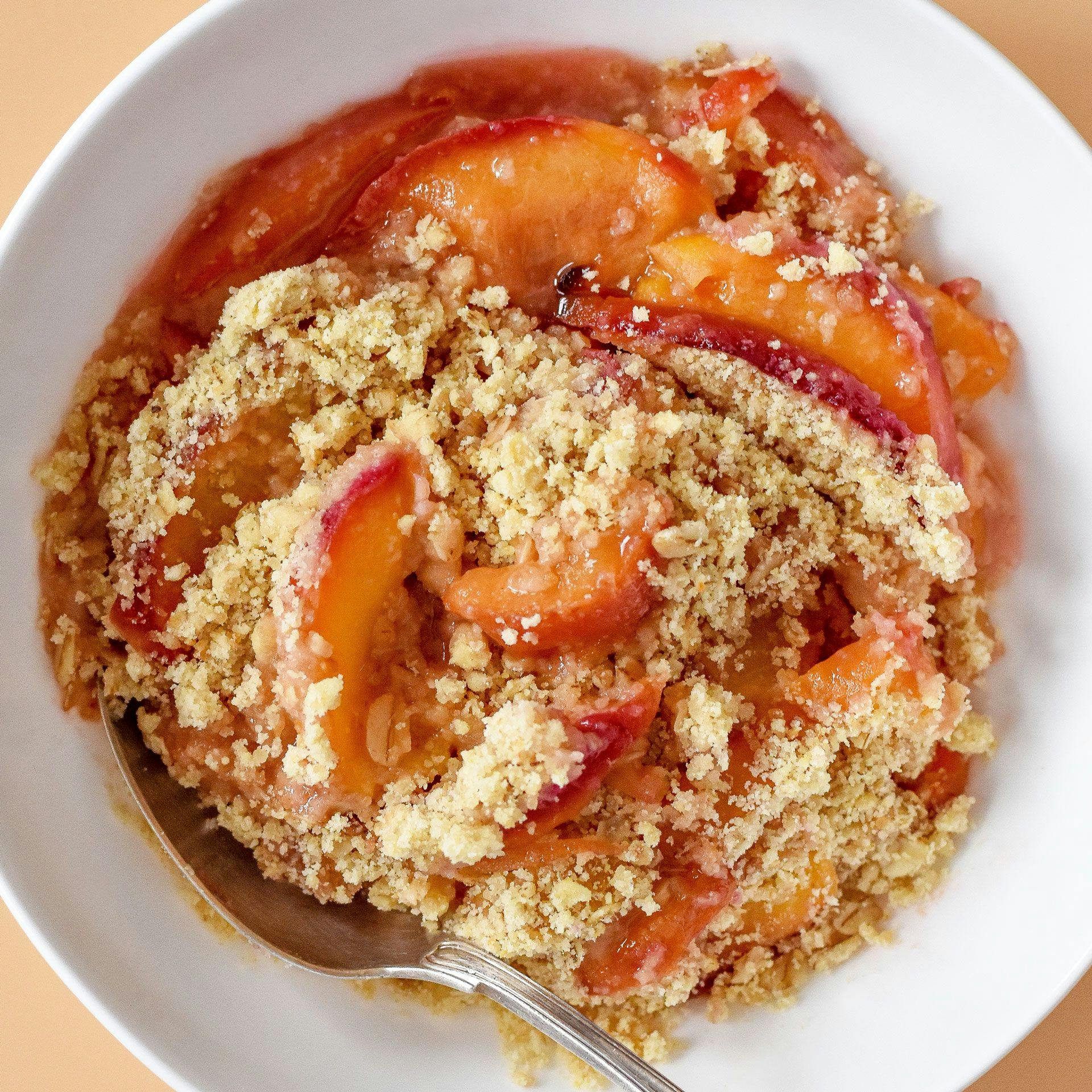 peach crumble in white bowl with spoon