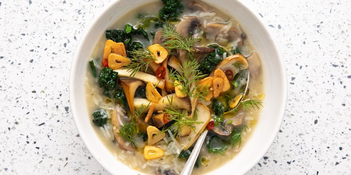 mushroom, rice and kale soup in white bowl with spoon