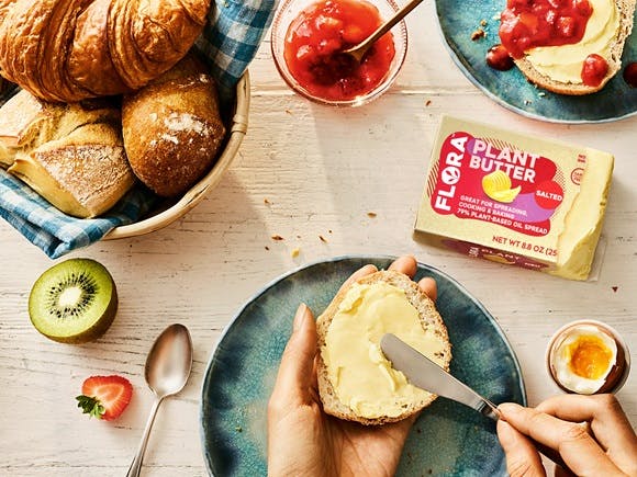 Flora butter spread on toast on table with jam and fruit.