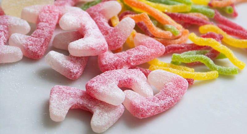 Close up image of sweets on a table, in front are fizy jelly fangs and there are fizzy worms in the background.