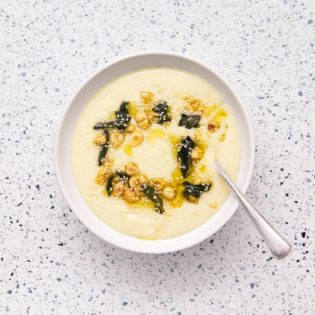 creamy cauliflower soup with sage and hazelnuts in white bowl with spoon