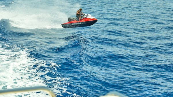 A man on a jet ski jumps over a wave. Taken from the back of a charter yacht