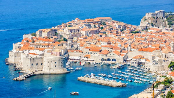 The stone city walls and red rooftops overlook yachts in the harbour of Dubrovnik old town, Croatia.
