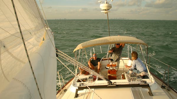 Three adult friends relax on a chartered yacht as they sail choppy seas in the sunshine 