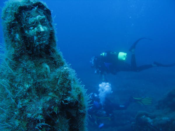A scuba diver swims past the submerged statue of Maddalena of the abyss, Italy