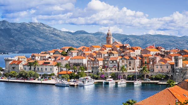 Red rooftops and old stone walls of Korcula Island, Croatia. A catamaran and two yachts are moored in the harbour
