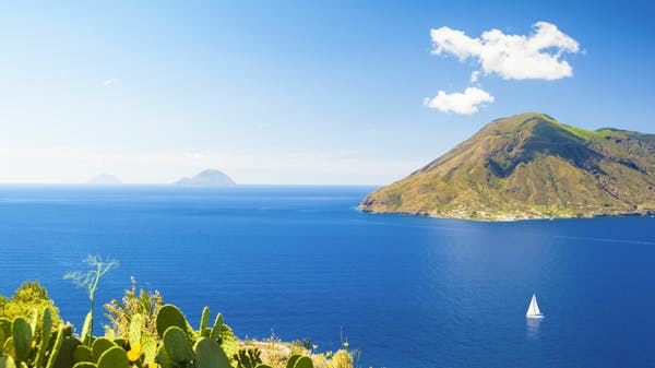 Yacht sails past the green coastline of Lipari in the Aeolian Islands, Sicily, Italy