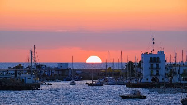 Sunset over Mogan harbour in Gran Canaria. Yachts are moored beside white buildings
