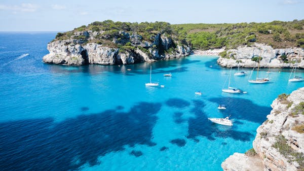 Yachts anchored in bright blue water in the rocky cove of Cala Macarella on Minorca, Balearic Islands, in Summer