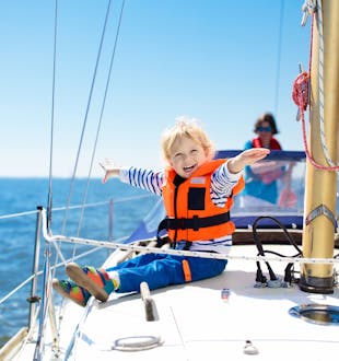 Kids sail on a charter yacht in the Mediterranean sea. A little boy smiles in safe child's life jacket while sitting on deck.
