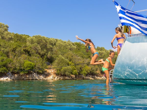 Children jump from a charter yacht in the sunshine with a Greek flag waving