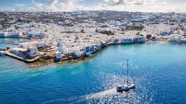 Aerial view of a yacht sailing on clear blue waters towards Mykonos island in the Cyclades, Greece