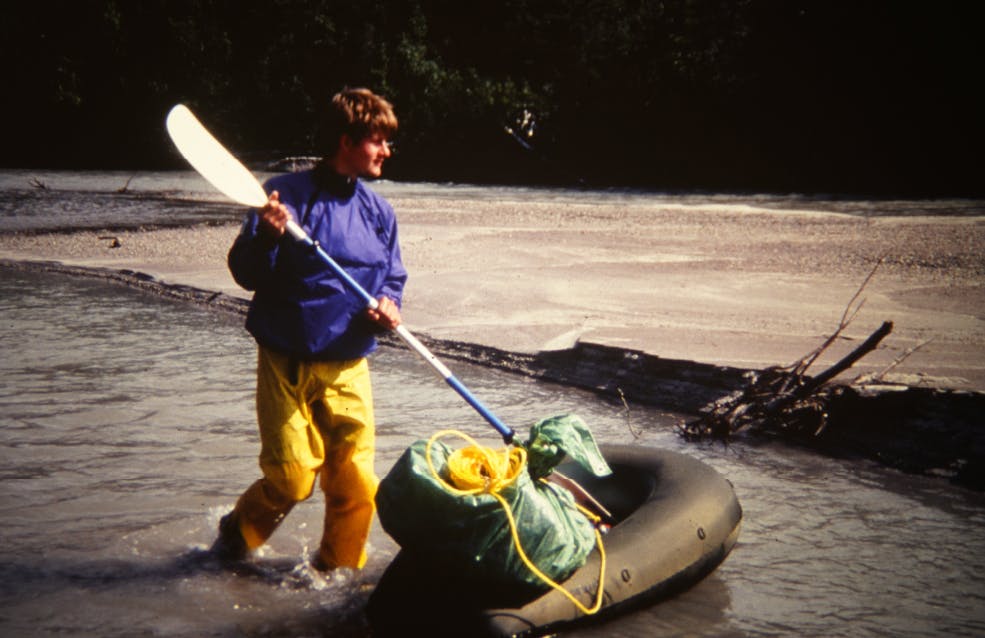 Scanned photograph of man in river with early packraft model and paddle