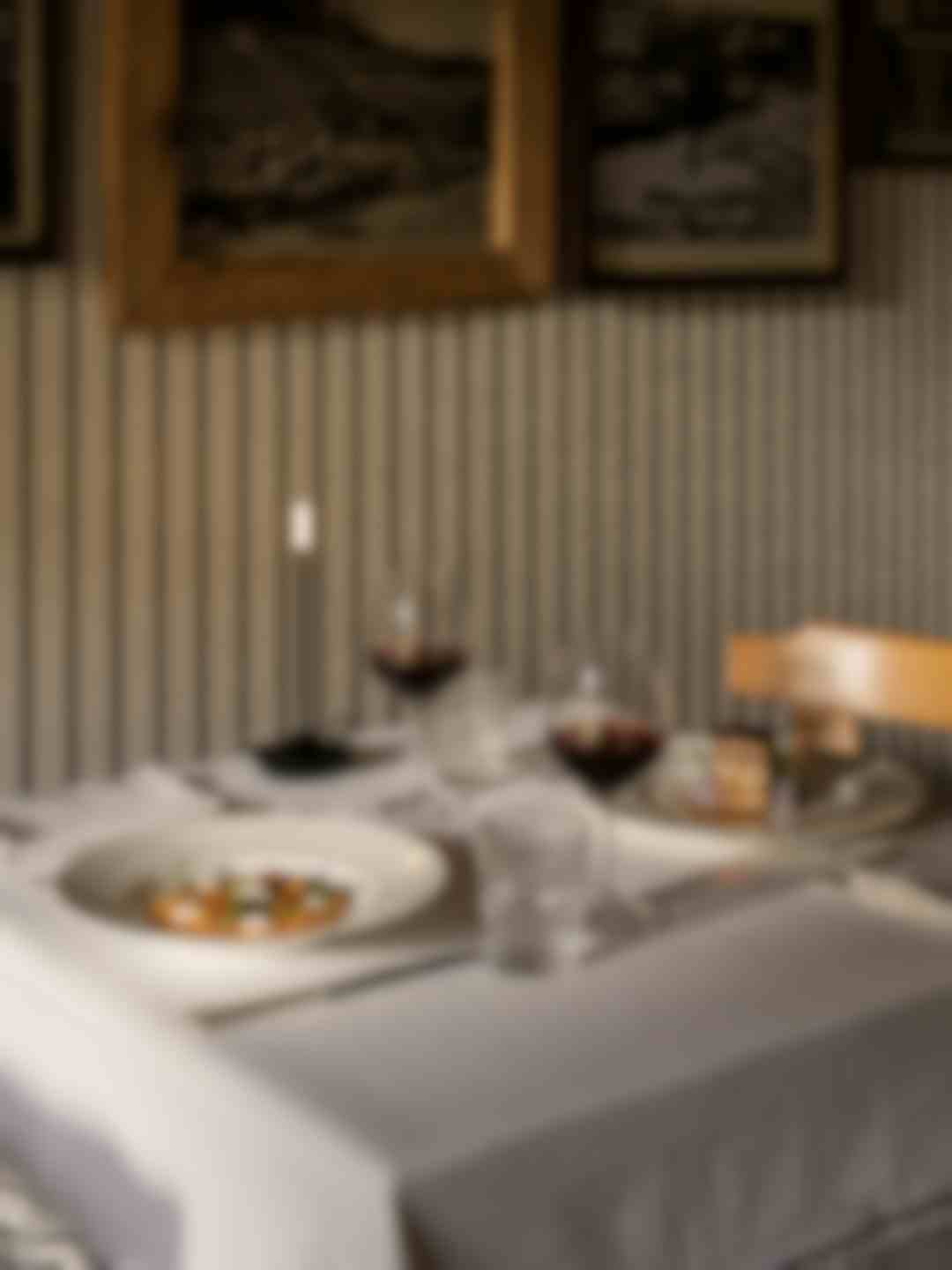 Tavolo ristorante con piatti gourmet, calici di vino rosso e candele accese, parete decorata con foto storiche d'epoca