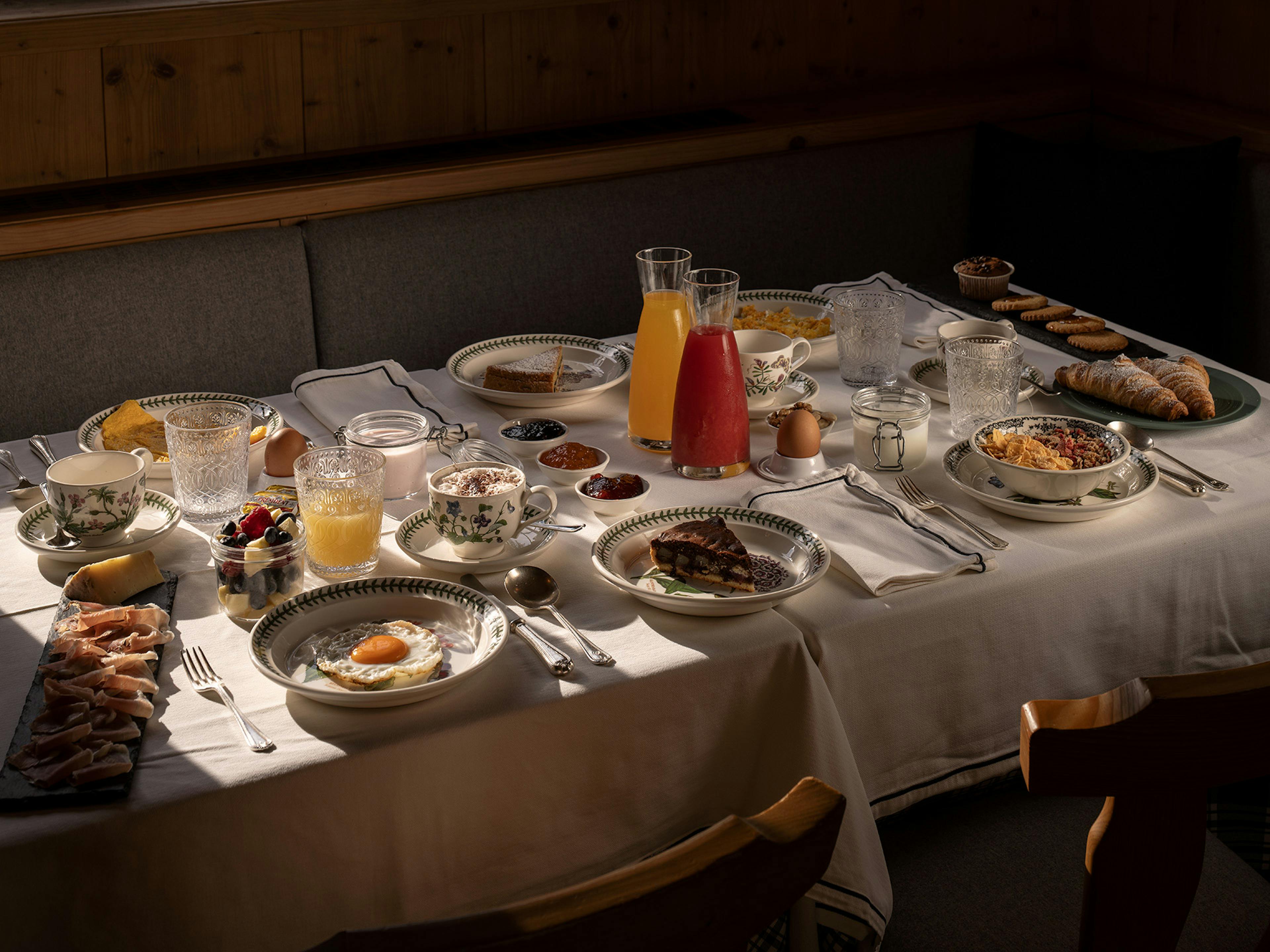 Ricca colazione continentale con uova, prosciutto crudo, croissant, marmellate, succhi freschi e yogurt su tavola apparecchiata