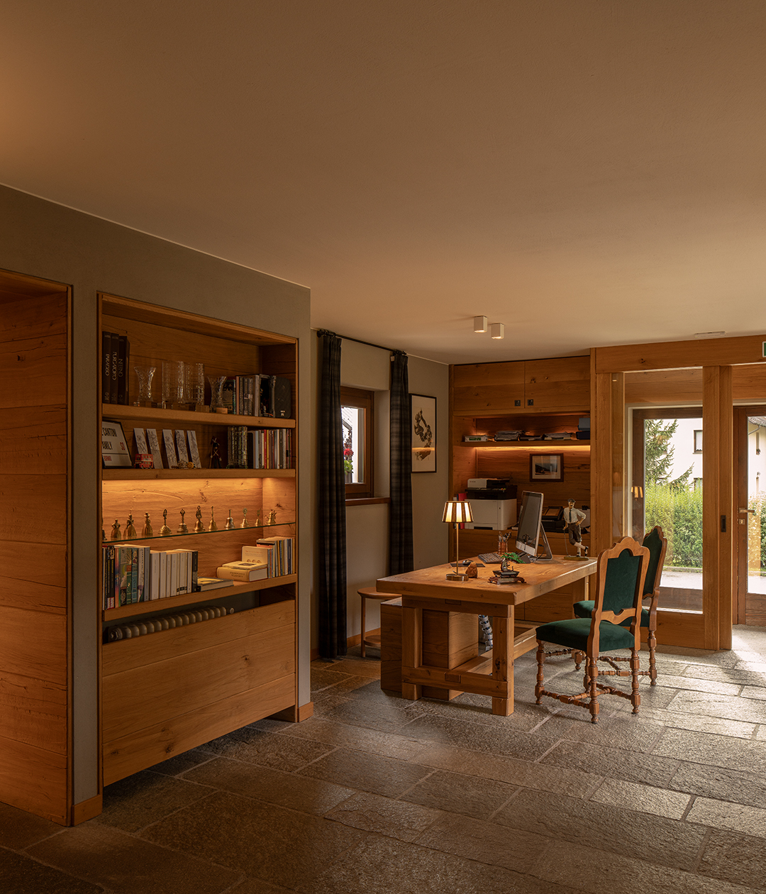 Zona pranzo interna con panca rivestita in velluto verde, libreria e vista sul soggiorno con ampie vetrate