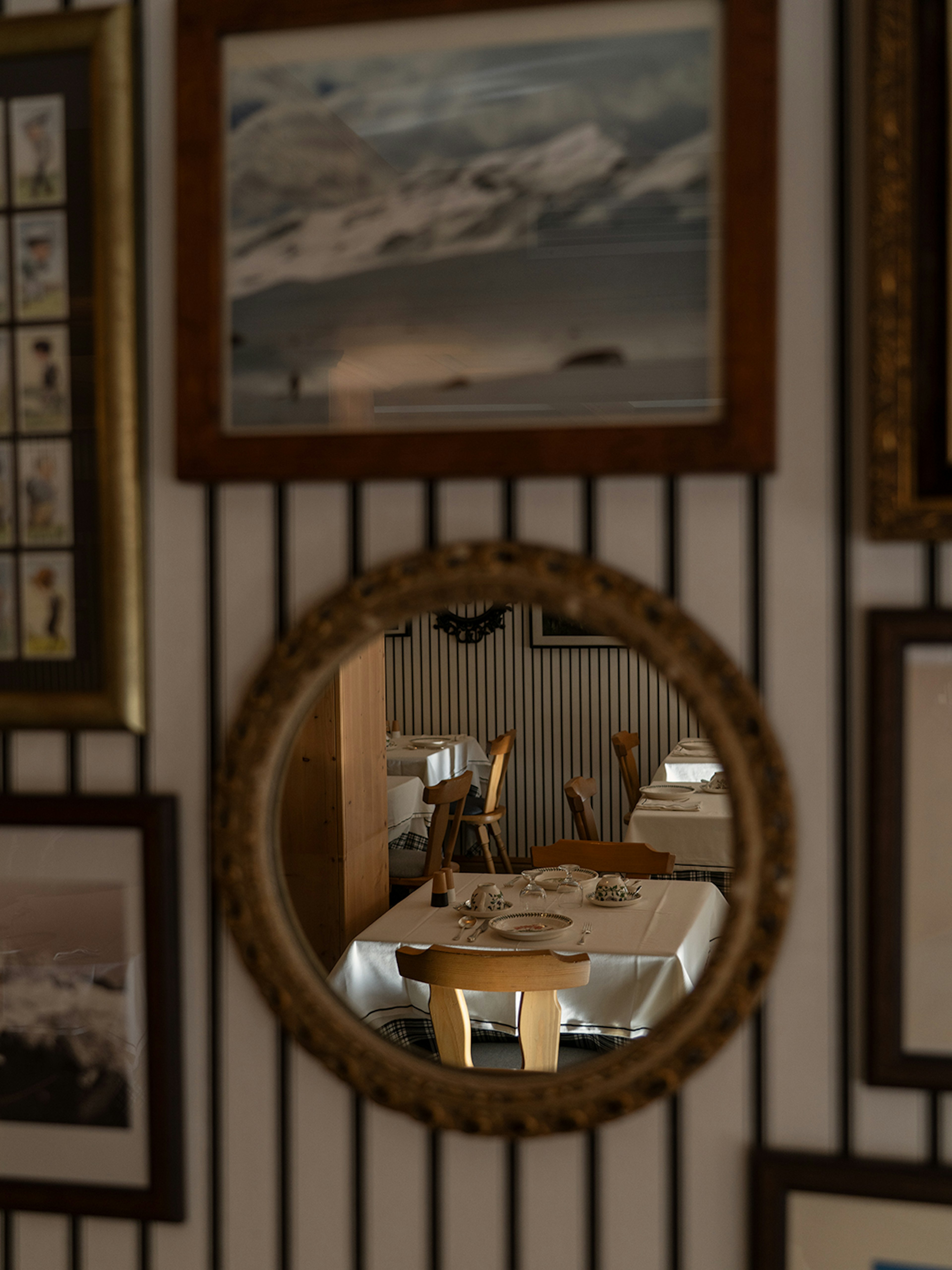 Sala ristorante dell'hotel vista attraverso specchio rotondo antico, tavoli apparecchiati con tovaglie bianche e sedie in legn