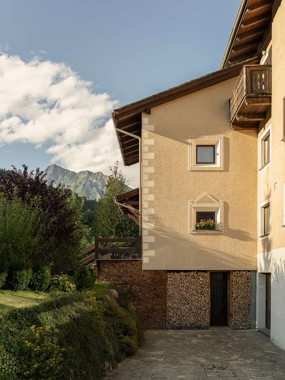 Casa tradizionale alpina con balcone in legno, legna accatastata e vista sulle montagne dolomitiche