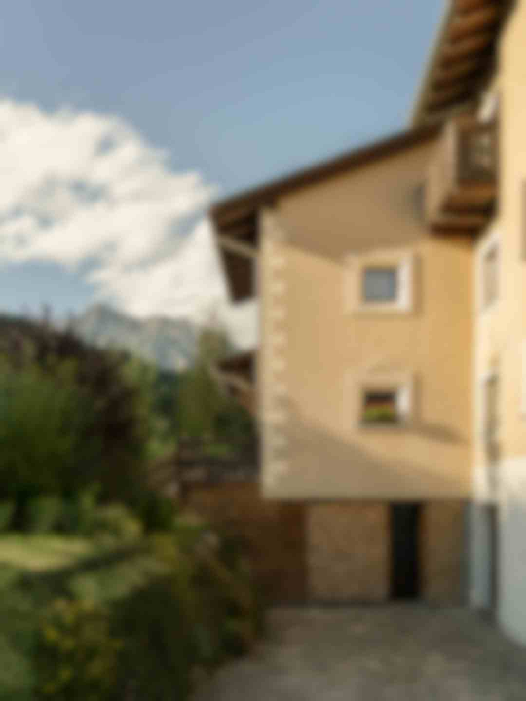 Casa tradizionale alpina con balcone in legno, legna accatastata e vista sulle montagne dolomitiche
