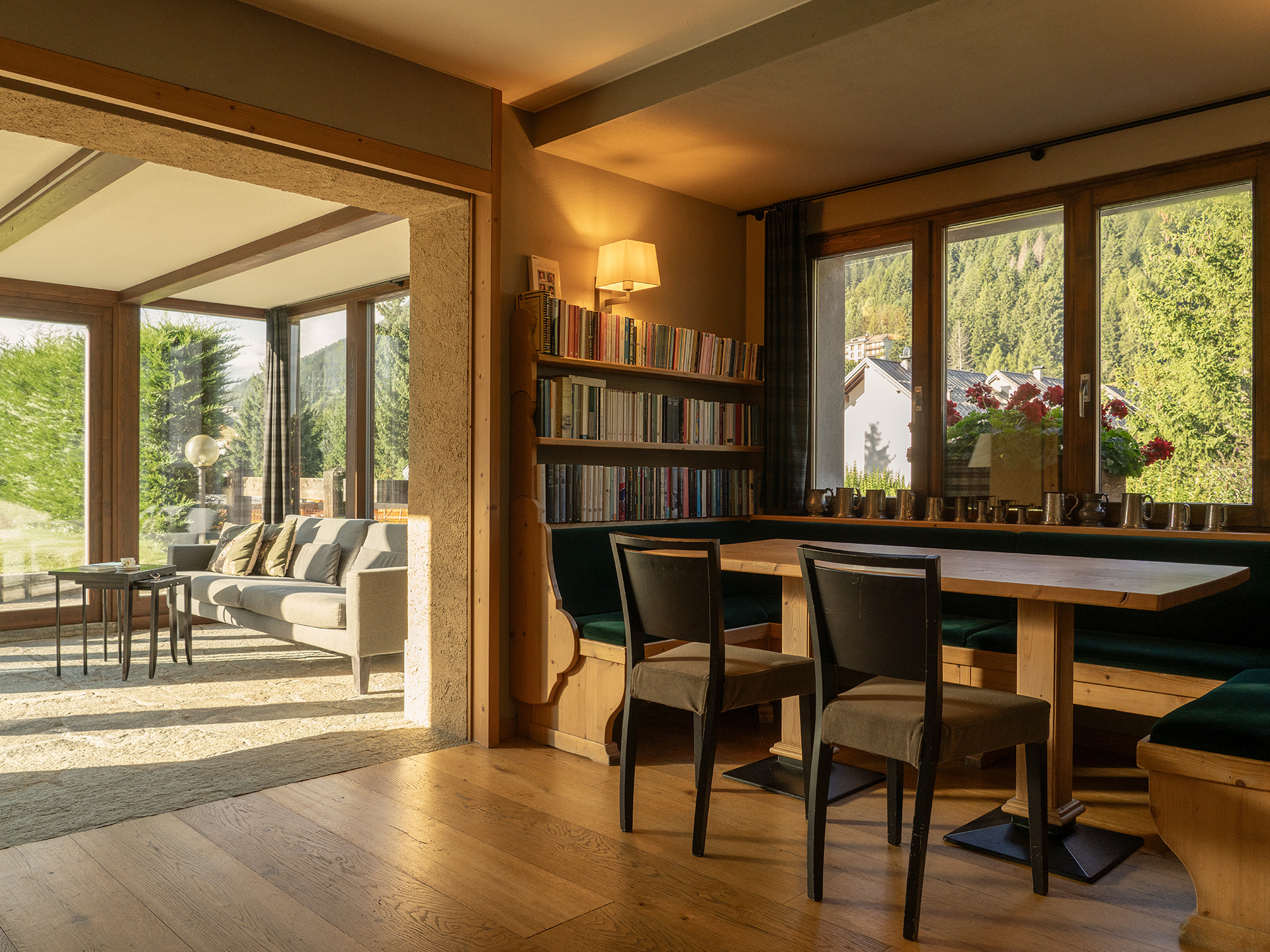 Zona salotto interna con panca rivestita in velluto verde, libreria e vista sul soggiorno con ampie vetrate