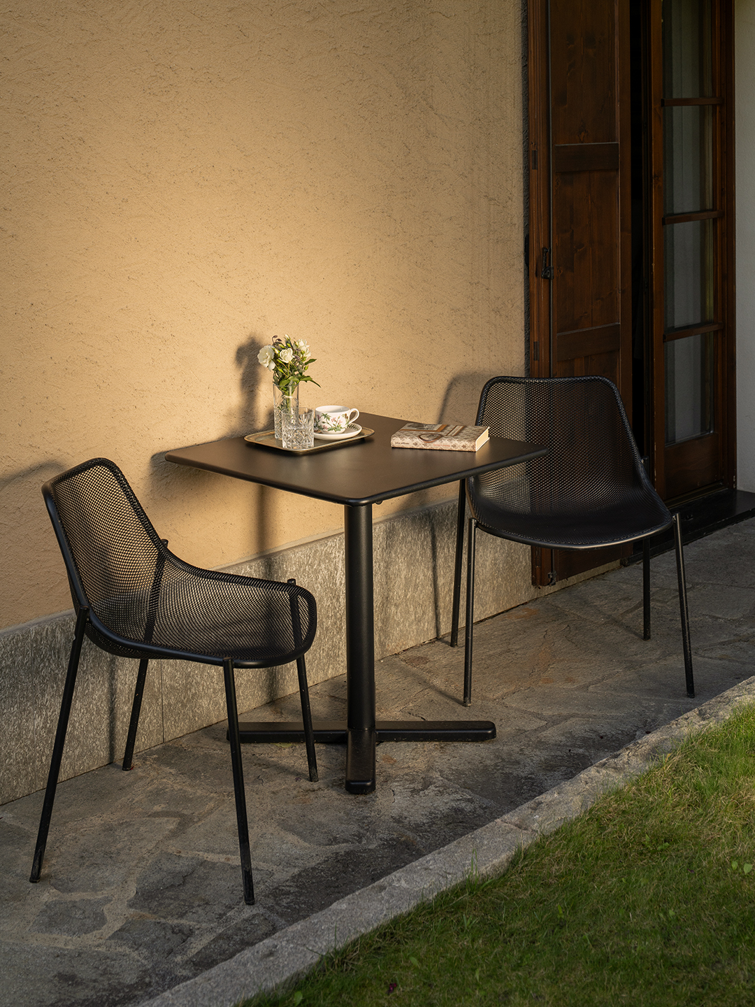 Tavolino da esterno con sedie nere su patio in pietra, illuminato dalla luce calda del tramonto