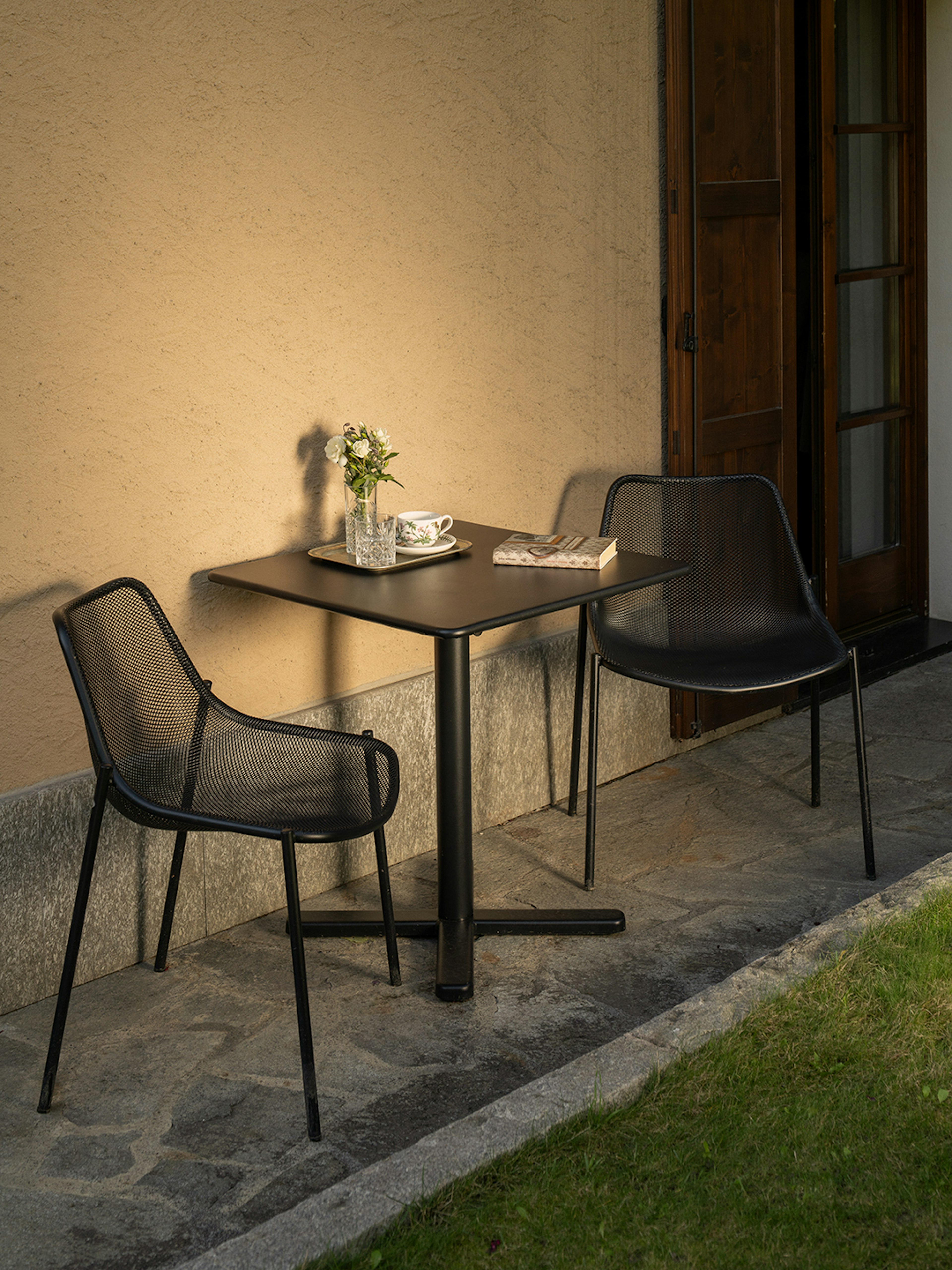 Tavolino da esterno con sedie nere su patio in pietra, illuminato dalla luce calda del tramonto