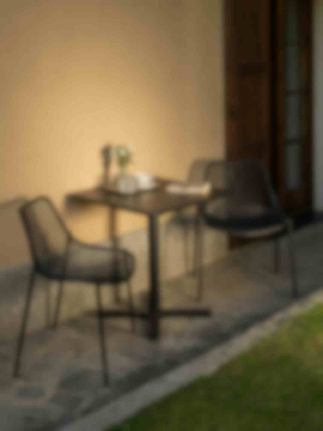 Tavolino da esterno con sedie nere su patio in pietra, illuminato dalla luce calda del tramonto