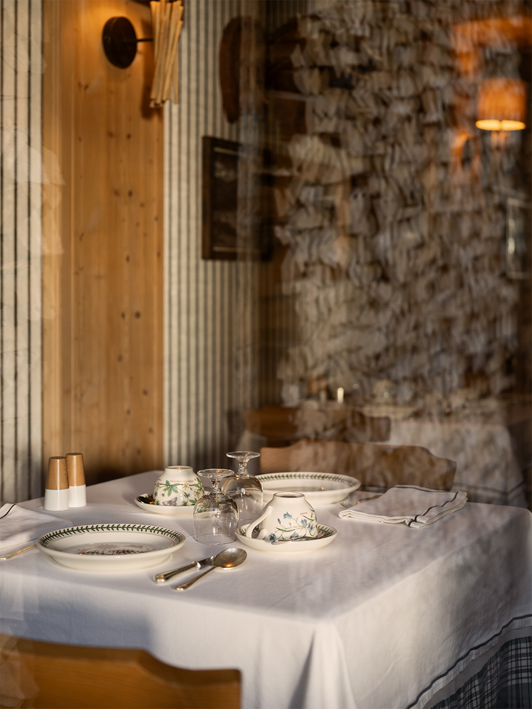 Tavola apparecchiata con tovaglia bianca e parete in pietra a vista, atmosfera rustica montana